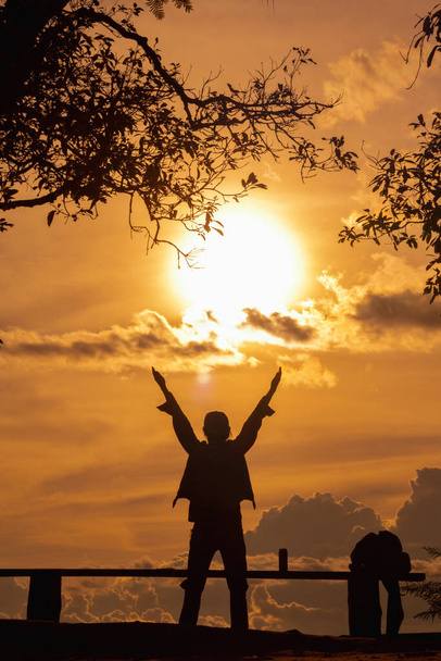 Uma silhueta de um jovem com as duas mãos erguidas acima da cabeça e orando a Deus com sua fé e poder sobre um fundo embaçado da bela vista do sol da manhã. - Foto, Imagem