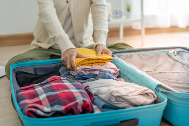Travel bags for vacation trips. A young woman prepares clothes and personal items to put in her suitcase. Pack your bags before traveling - 写真・画像