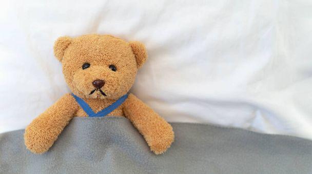 Sad and disappointed teddy bear lying in bed. Teddy bear is sick and crying. - Photo, Image