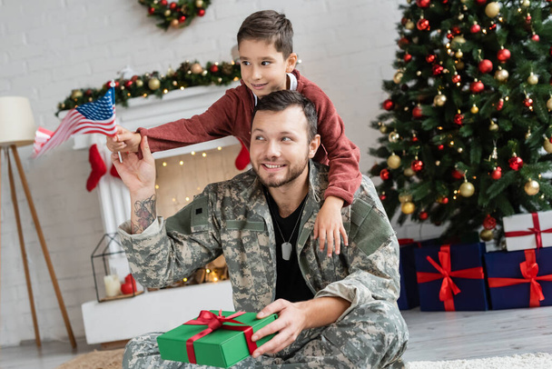 Gülümseyen babasının yanında bayrak tutan çocuk Noel hediyesiyle oturuyor. - Fotoğraf, Görsel