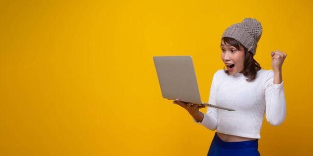 オレンジ色の背景にコンピュータに興奮し、驚きの美しいアジアの女性。女性はオンラインショッピングサイトで販売を見た. - 写真・画像