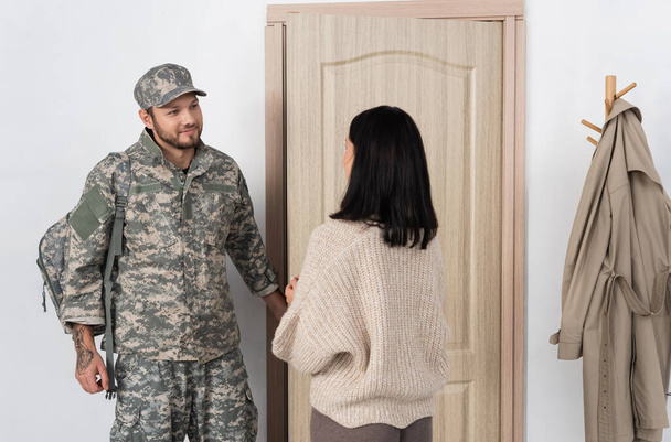 μελαχρινή γυναίκα που συναντιέται χαμογελώντας αξύριστος σύζυγος με στρατιωτική στολή που επιστρέφει σπίτι - Φωτογραφία, εικόνα