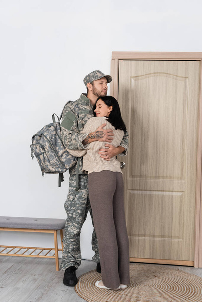 чоловік у військовій формі, що обіймає щасливу дружину біля вхідних дверей вдома
 - Фото, зображення