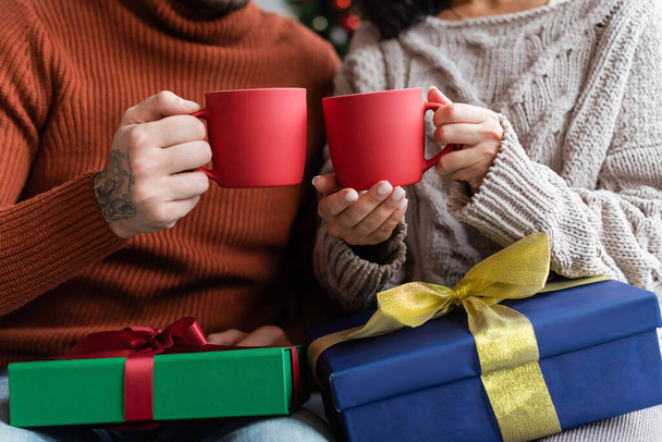 oříznutý pohled na pár drží poháry teplého kakaa v blízkosti vánočních dárečků - Fotografie, Obrázek