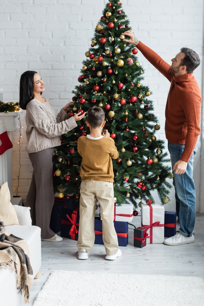 οικογενειακή διακόσμηση ερυθρελάτης με μπάλες Χριστουγέννων κοντά κουτιά δώρων στο σαλόνι - Φωτογραφία, εικόνα