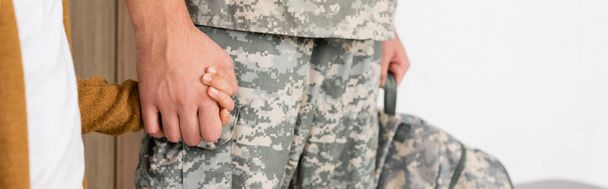 καλλιεργημένη άποψη του ανθρώπου με στρατιωτική στολή κρατώντας τα χέρια με το γιο στο σπίτι, πανό - Φωτογραφία, εικόνα