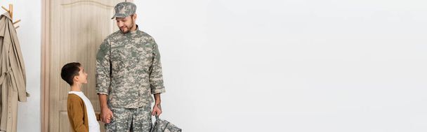 militaire avec sac à dos tenant la main avec son fils le rencontrant près de la porte à la maison, bannière - Photo, image