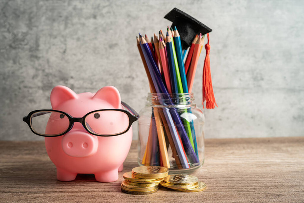 Pigging bank wearing eyeglass with colorful pencils; saving bank education concept. - Фото, изображение