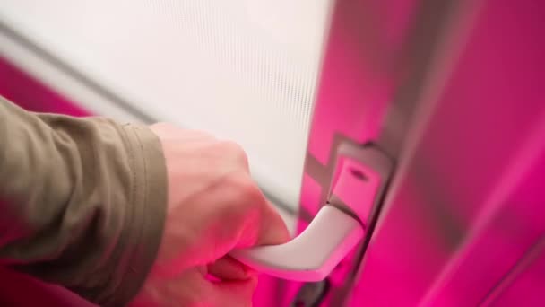 Uma mão abre um close-up da alça de uma porta de plástico branco sob uma luz de fundo rosa brilhante e saturada. Saia da discoteca. Imagens 4k de alta qualidade - Filmagem, Vídeo