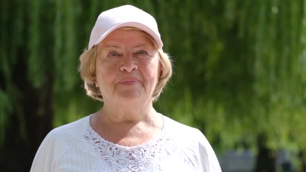 Ritratto di donna anziana in berretto all'aperto, pensionato che guarda la macchina fotografica. Giornata estiva. Rallentatore - Filmati, video