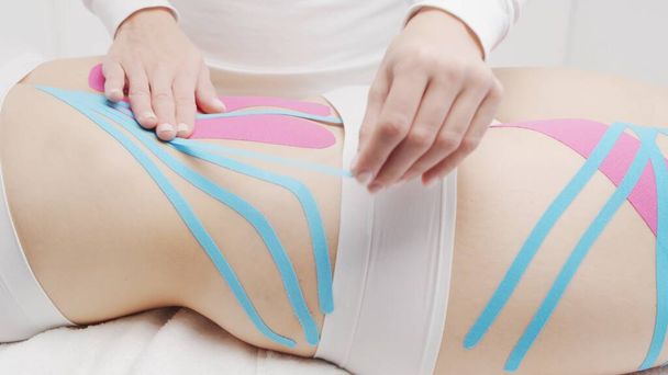 Therapist is applying tape to beautiful female body. Physiotherapy, kinesiology and recovery treatment. - Φωτογραφία, εικόνα