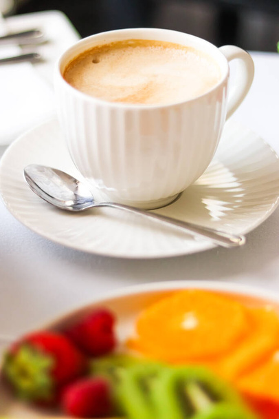 Завтрак и роскошь, чашка кофе с молоком и фруктовым блюдом на обслуживаемом столе для гостеприимства и гастрономии брендинга - Фото, изображение