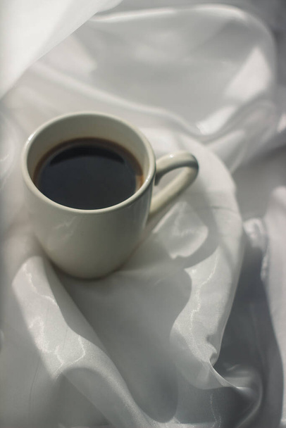 tazza di caffè al mattino. caffè espresso. Porridge di caffè su uno sfondo bianco una tazza di caffè su un panno bianco. raggi di sole su una tazza di caffè - Foto, immagini