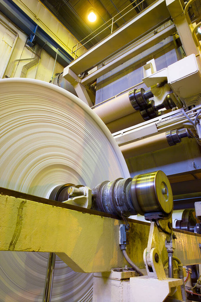 Μεγάλα ρολά χαρτιού που βγαίνουν από τα μηχανήματα σε εργοστάσιο χαρτοποιίας. - Φωτογραφία, εικόνα