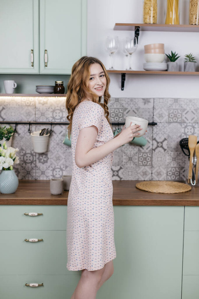 Hermosa chica en pijama en la cocina con una gran taza, colores pastel, humor de la mañana - Foto, imagen