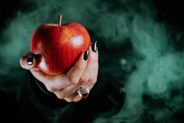 Woman as witch offers red apple as symbol of temptation, poison. Fairy tale, white snow wizard concept. Spooky halloween, cosplay. Smoke, haze background. High quality photo - Fotografie, Obrázek