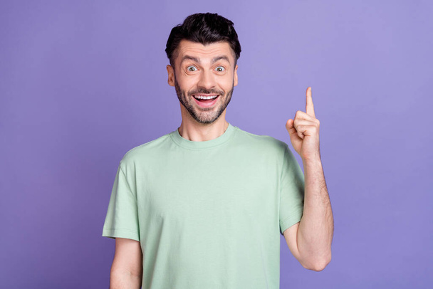 Portrait of positive satisfied impressed man with brunet hairdo dressed t-shirt get idea finger up isolated on purple color background. - Photo, image