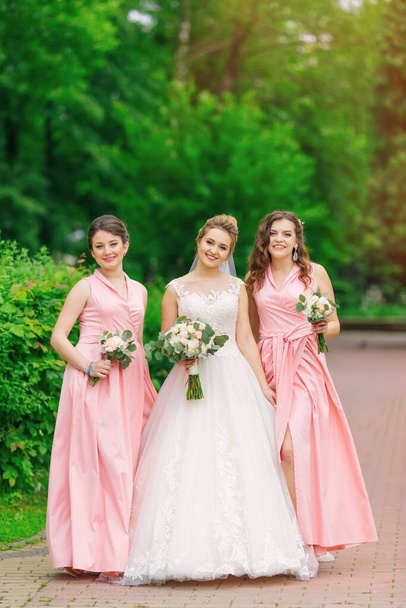 Невеста с подружками невесты в парке в день свадьбы. девушки держат свадебные букеты. - Фото, изображение
