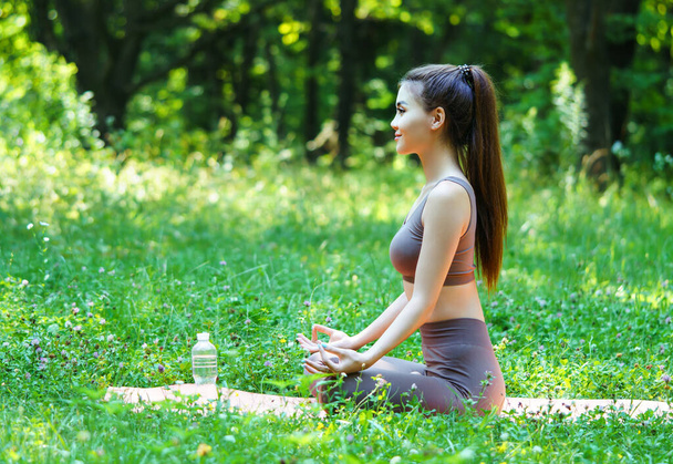 Beautiful asian woman practicing yoga, sitting in a lotus pose at the meadow. - Zdjęcie, obraz