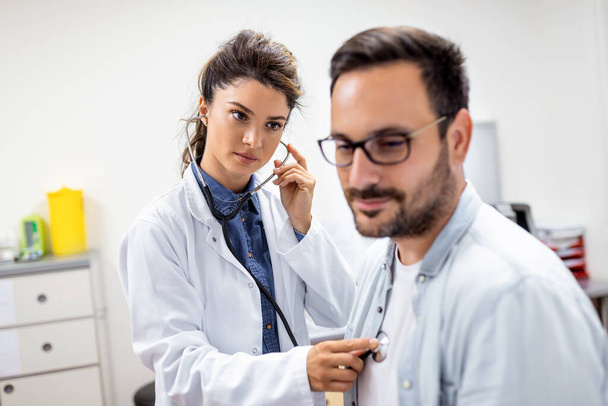 Young female doctor listen to male patient heart chest with stethoscope at clinic meeting. Woman GP checkup examine man client with phonendoscope. healthcare concept. - Foto, Bild