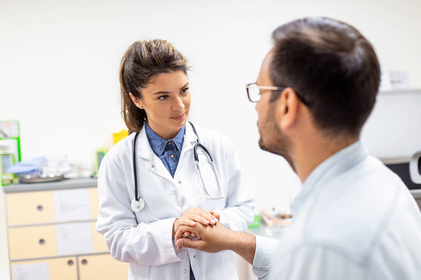 Young female doctor hold hand of caucasian man patient give comfort, express health care sympathy, medical help trust support encourage reassure infertile patient at medical visit - Фото, зображення