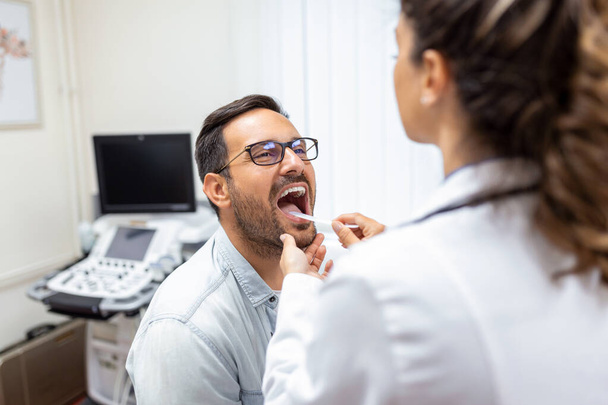 Doctor using inspection spatula to examine patient throat. ENT doctor doing throat exam. patient opened his mouth to throat check-up - Photo, Image
