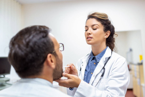Male patient opening his mouth for the doctor to look at his throat. Female doctor examining sore throat of patient in clinic. Otolaryngologist examines sore throat of patient. - Foto, Imagem
