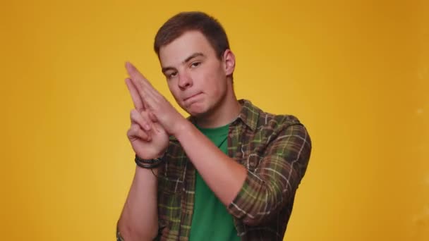 Happy teen man pointing around with finger gun gesture, looking confident, making choice, shooting killing with hand pistol right on target. Young adult guy boy isolated on yellow studio background - Footage, Video