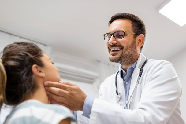 medicine, healthcare and medical exam concept - doctor checking patient's tonsils at hospital. Endocrinologist examining throat of young woman in clinic - Photo, Image