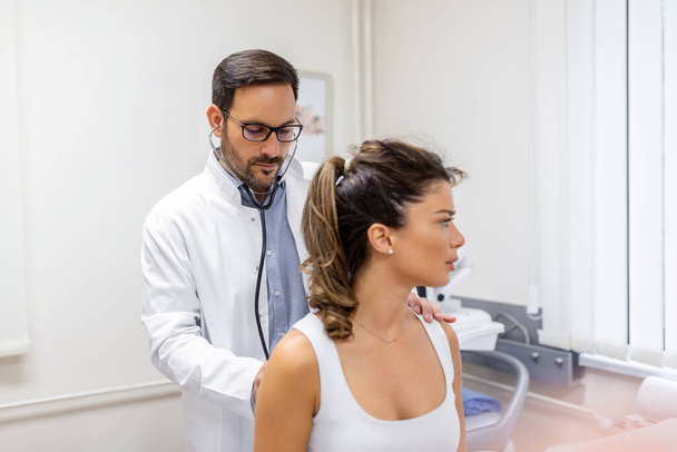 Aufnahme eines Arztes, der eine junge Frau mit einem Stethoskop untersucht, Lets have a hear to your Lungen - Foto, Bild