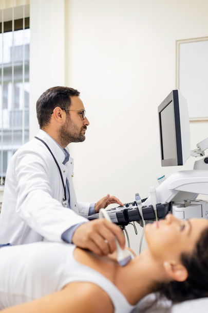 Der männliche Endokrinologe macht eine Ultraschalluntersuchung bei einer Patientin in einer Ultraschallpraxis. Ultraschalldiagnostik der Schilddrüse. - Foto, Bild