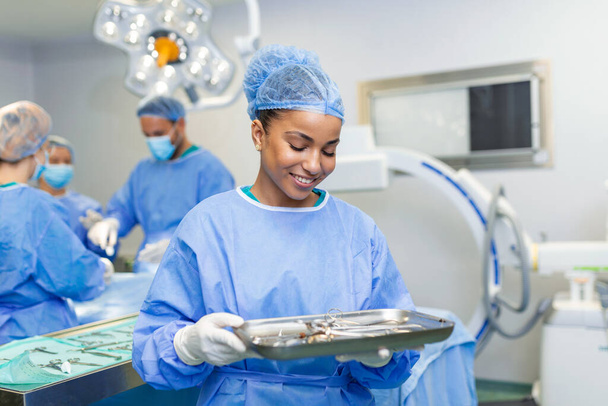 Portret kobiety pielęgniarki chirurga LUB członka personelu ubranego w fartuch chirurgiczny fartuch maska i siatka na włosy w sali operacyjnej szpitala dzięki czemu kontakt wzrokowy uśmiecha się zadowolony patrząc w kamerę - Zdjęcie, obraz