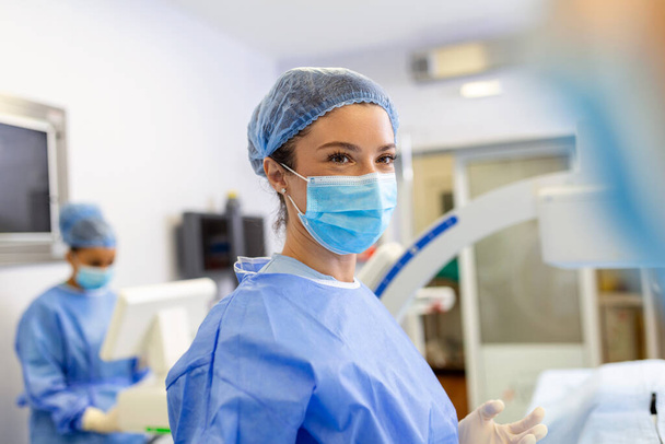 Female surgeon with surgical mask at operating room. Young woman doctor in surgical uniform in hospital operation theater. - Foto, afbeelding