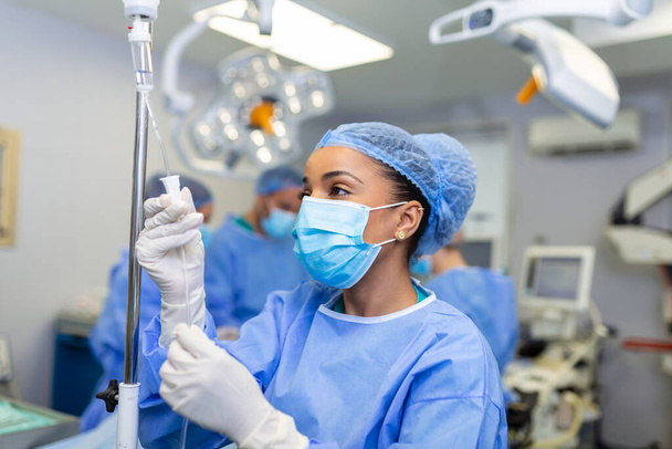 African american female Doctor in the operating room putting drugs through an IV - surgery concepts - 写真・画像