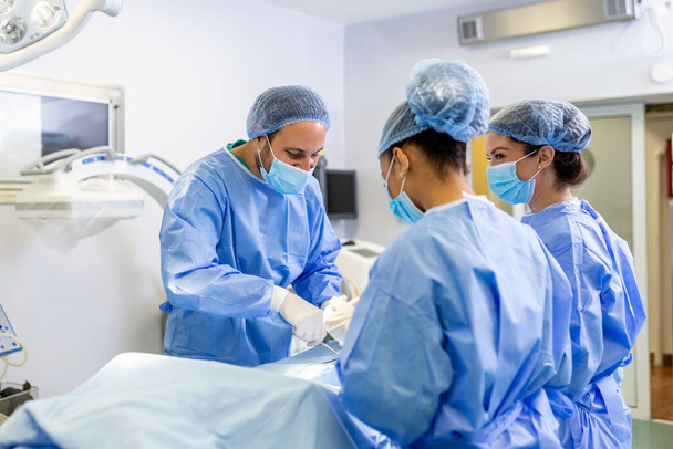 Группа врачей срочно проводит хирургическую операцию и помогает пациенту в больнице. Медицинская команда, выполняющая хирургическую операцию в яркой современной операционной - Фото, изображение