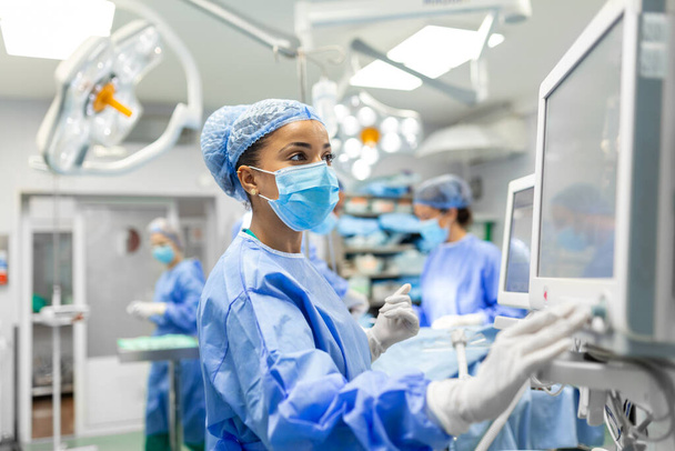 病院で手術前に患者を鎮静させながら、保護ギアチェックモニターを装着した手術室で働く麻酔医 - 写真・画像