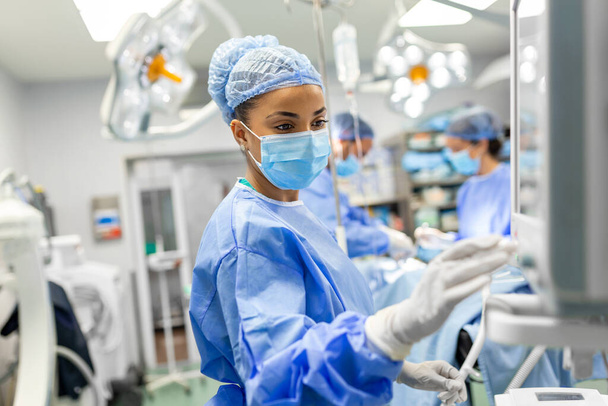 Portrait of a young female doctor in scrubs and a protective face mask preparing an anesthesia machine before an operation - Photo, image