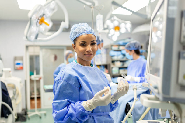 Portret van een jonge vrouwelijke arts in scrubs en een beschermend gezichtsmasker die een anesthesiemachine voorbereidt voor een operatie - Foto, afbeelding