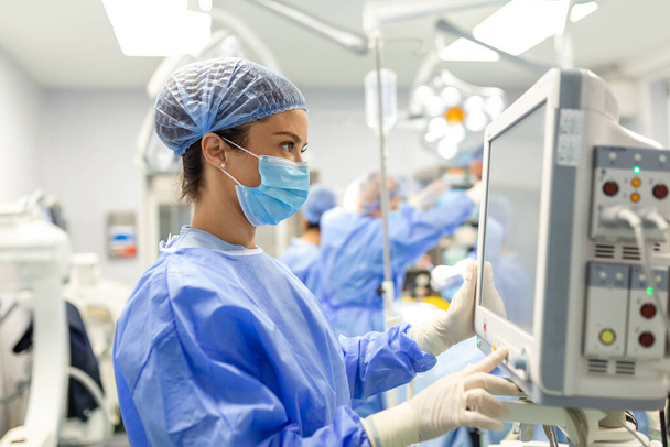 Анестезиолог отслеживает жизненно важные функции организма во время кардиохирургии. Хирург смотрит на медицинский монитор во время операции. Врач проверяет состояние здоровья пациента. - Фото, изображение