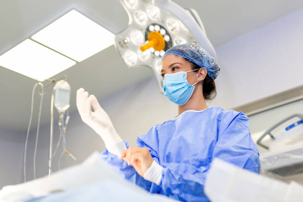 Porträt einer schönen Ärztin, die im Operationssaal medizinische Handschuhe anzieht. Chirurg im modernen Operationssaal - Foto, Bild