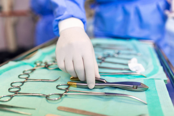 Chirurg nimmt chirurgisches Werkzeug aus Tablett. Chirurg bereitet sich auf Operation im Operationssaal vor. Er liegt im Krankenhaus. - Foto, Bild