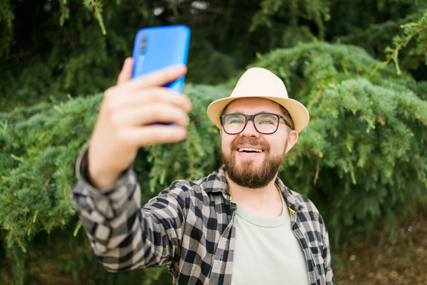 Man taking selfie portrait over palm tree background - Happy millennial guy enjoying summer holidays in city - Youth and technologies. - Zdjęcie, obraz