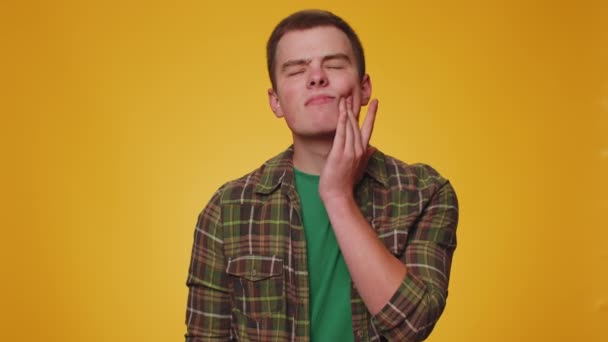 Teenager mladý muž dotýká bolavé tváře trpí zubní dutiny nebo zánět dásní čeká na návštěvu zubaře, onemocnění dásní. Dospělý chlapec vnitřní studio shot izolovaný sám na žlutém pozadí - Záběry, video