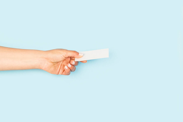 Main de femme tenant une carte personnelle blanche vierge sur un fond bleu clair avec espace de copie - Photo, image