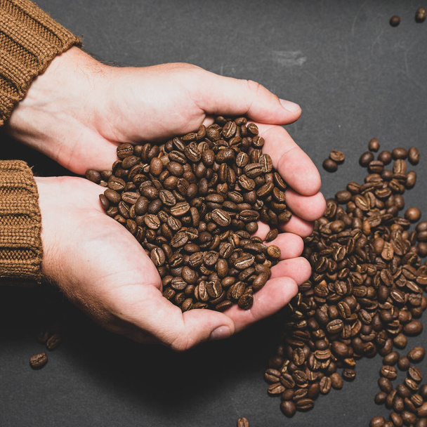 Male hands hold coffee on a dark background, coffee beans in hands. - Photo, Image