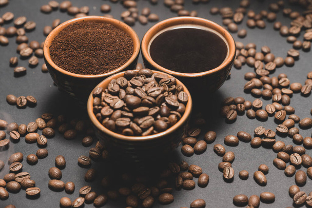 Freshly ground and brewed black coffee on a black background, three cups with steamed coffee. - Foto, Imagem