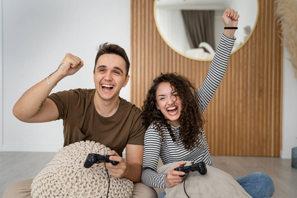 Dwie osoby para mężczyzna i kobieta chłopak i dziewczyna mąż i żona lub przyjaciele grać konsola gry wideo trzymać joystick kontroler szczęśliwy uśmiech emocjonalny gest wygrana reakcja rodzina skopiować przestrzeń - Zdjęcie, obraz