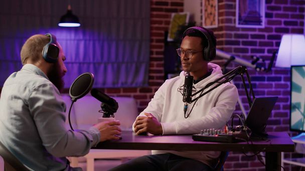 African american podcaster in interview with famous influencer greeting guest doing fist bump in home studio. Internet radio host meeting social media vlogger in live podcast in evening show. - Foto, afbeelding