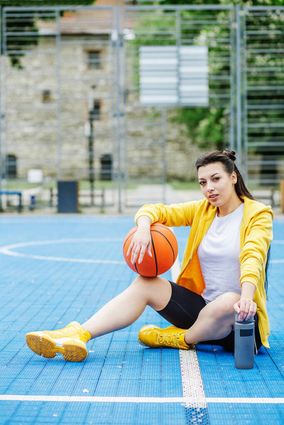 Reusable water bottle. Female athlete is resting during break on basketball court, drinking water. Sport and hobby concept. - Foto, Imagen