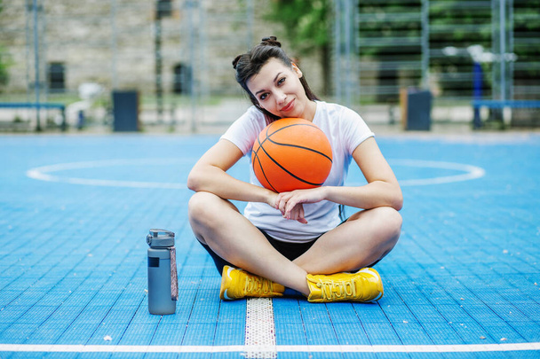 Багаторазова пляшка води. Жінка-спортсменка відпочиває під час перерви на баскетбольному майданчику, п'є воду. Концепція спорту та хобі
. - Фото, зображення